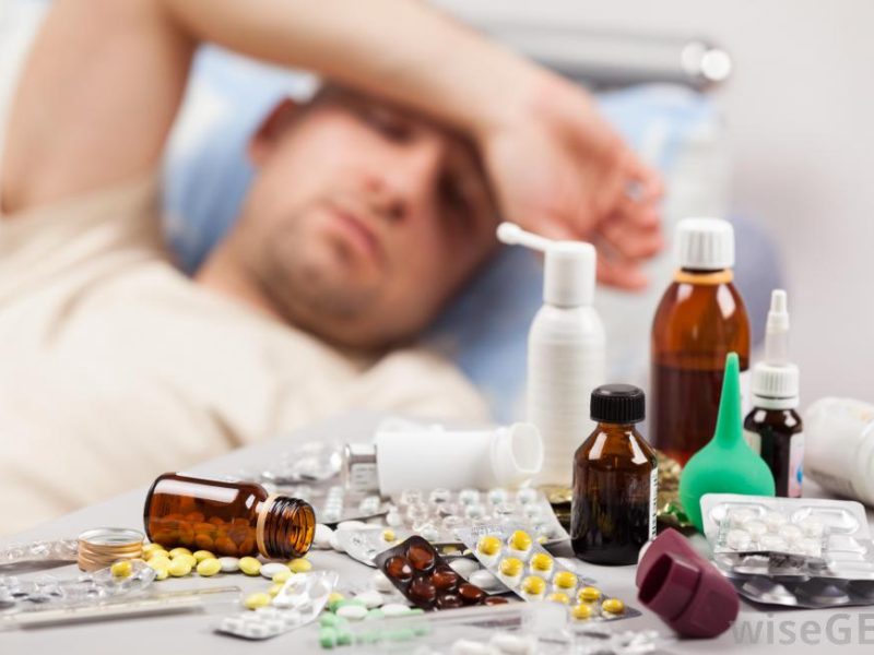 man-with-hand-over-his-head-feeling-ill-in-background-with-close-view-of-pills-and-medicine (1)